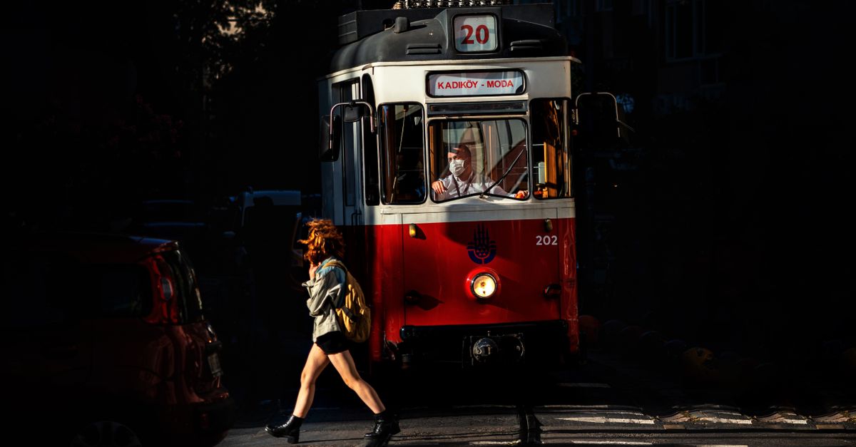 moda sostenible y estilo personal: Woman crossing in front of a vintage tram in Istanbul's Moda district at dusk.