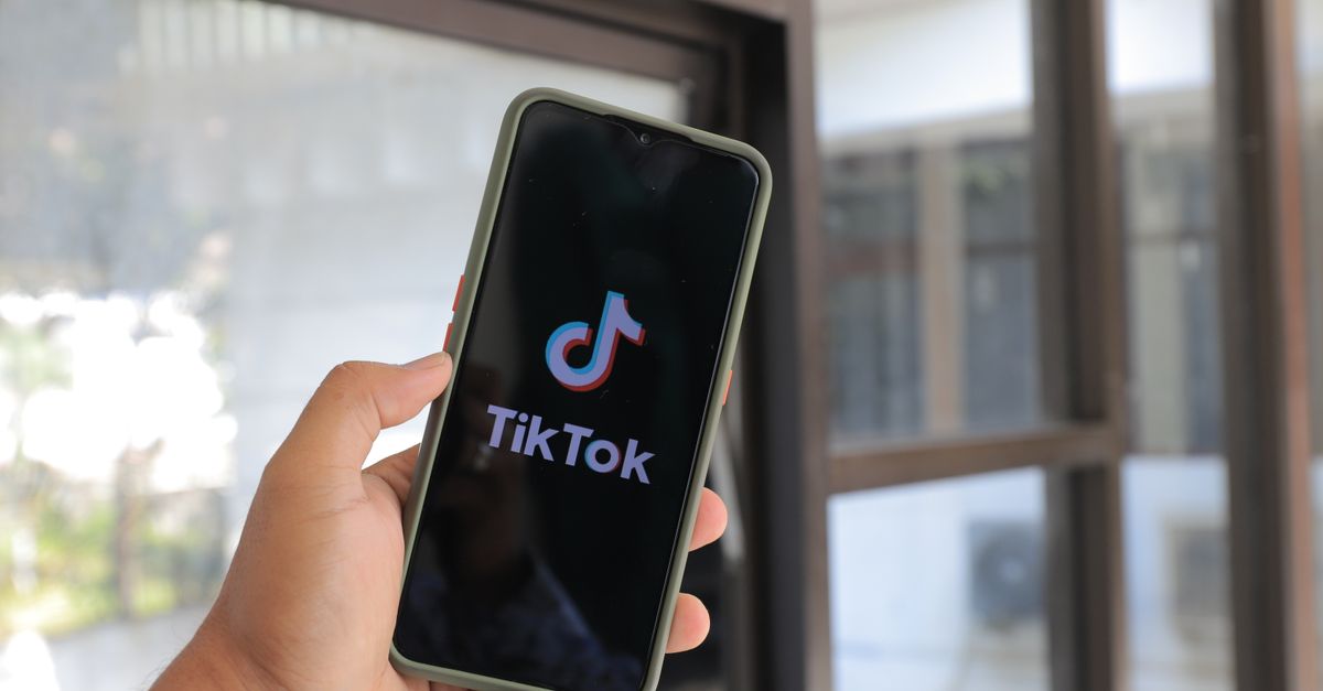 TikTok destrona a Google, Tendencia social media technology: Close-up of a hand holding a smartphone displaying the TikTok app indoors.