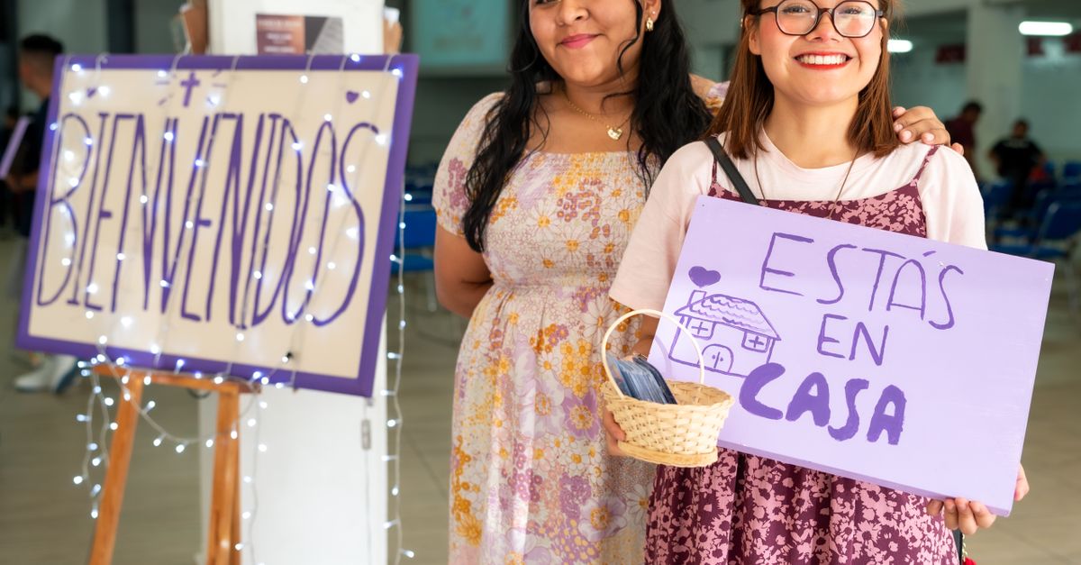 mascotas, cómo vivir con perritos en casa: Two women warmly greet visitors at a community event in Ciudad de México with signs saying 'Bienvenidos' and 'Estás en Casa'.
