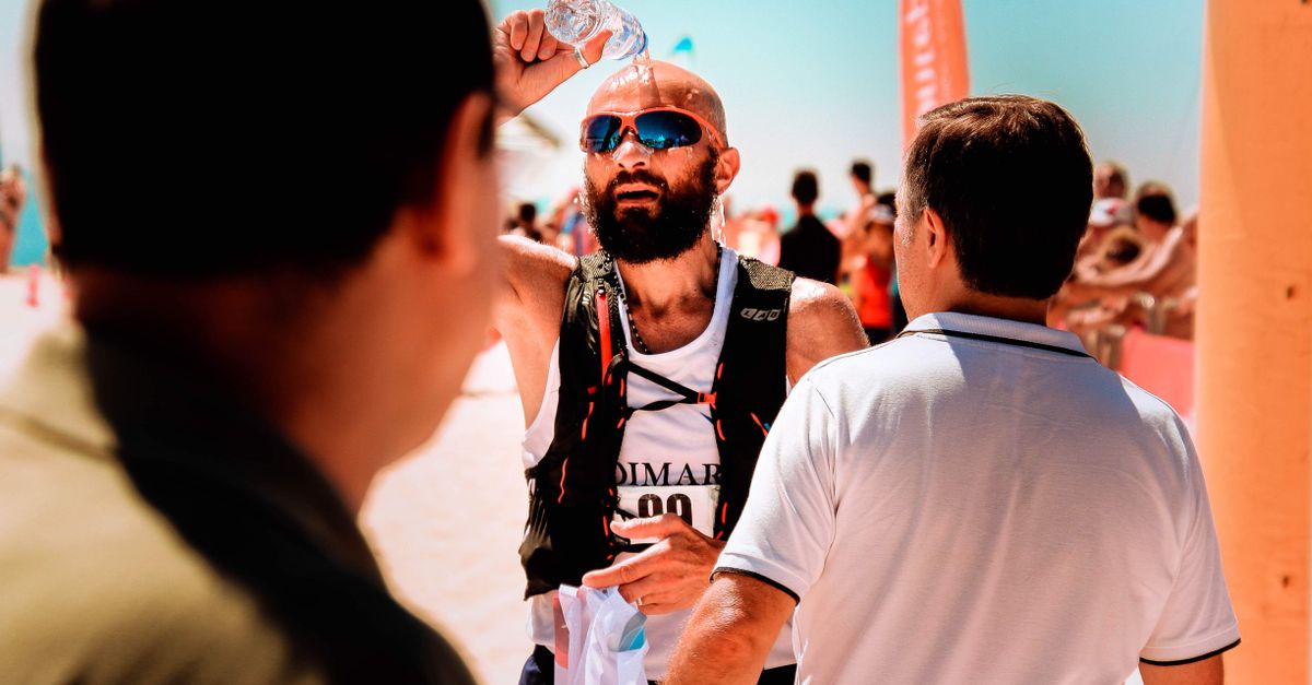 cómo prepararse para olas de calor sin descuidar la salud diaria: A male runner cools down with water during a summer marathon by the seaside.