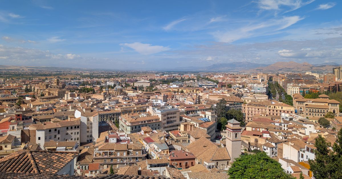 ciencia ciudadana contra el calor urbano: Aerial view of Granada, showcasing its historic architecture and distant Sierra Nevada Mountains under a clear blue sky.