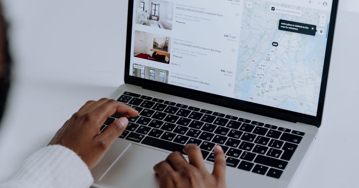 plataformas web de viajes con ofertas para viajar: Hands typing on laptop searching Airbnb for accommodation options with map view.