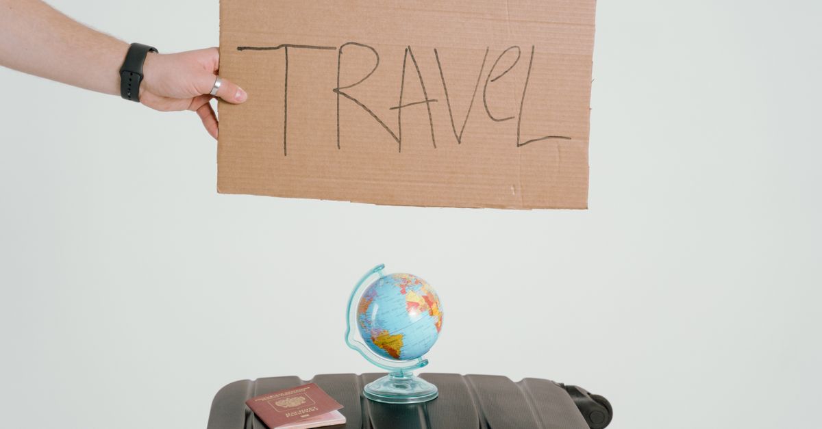 plataformas web de viajes con ofertas para viajar: A hand holds a travel sign above a globe and suitcase, symbolizing wanderlust.