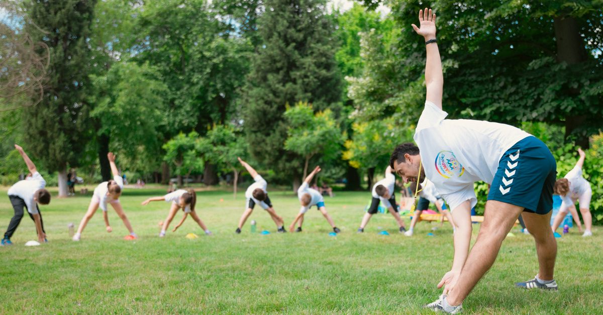 Cómo armar una rutina semanal de movimiento, sueño y alimentación que ayude a prevenir enfermedades crónicas bienestar practico educational neutral health: Kids stretching exercises in a park guided by a coach, promoting fitness and fun.