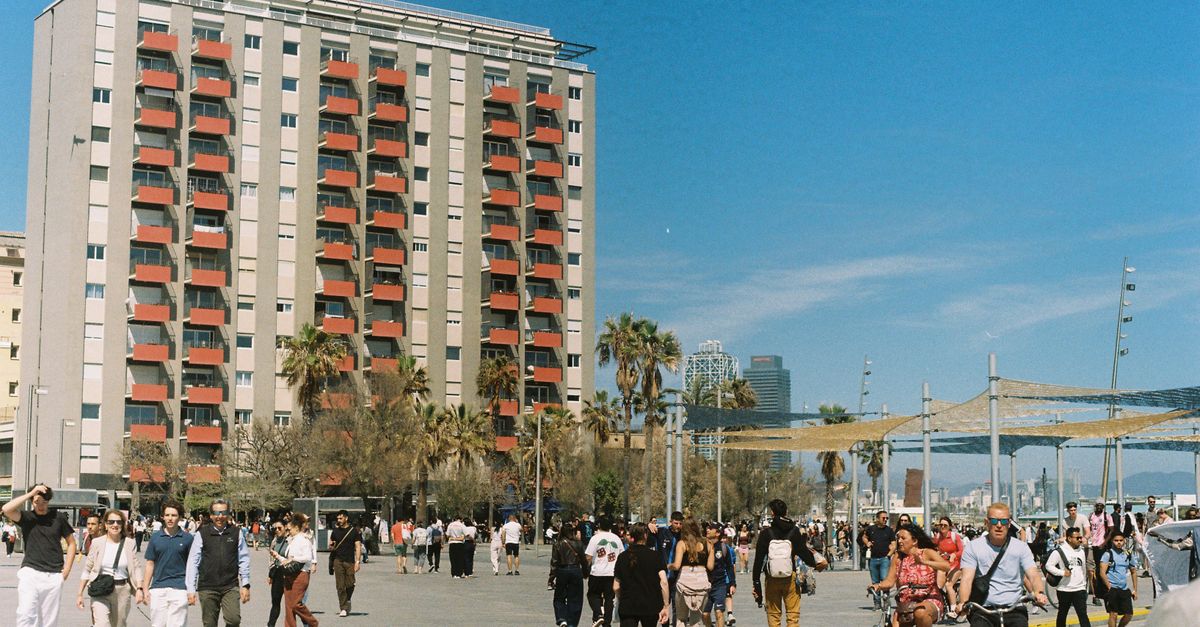 Vacaciones a destinos frescos: cómo planear un viaje cómodo, sostenible y fuera de temporada alta viajes inteligentes destination specific travel: Busy day in Barcelona with people walking and cycling by a residential building and palm trees.