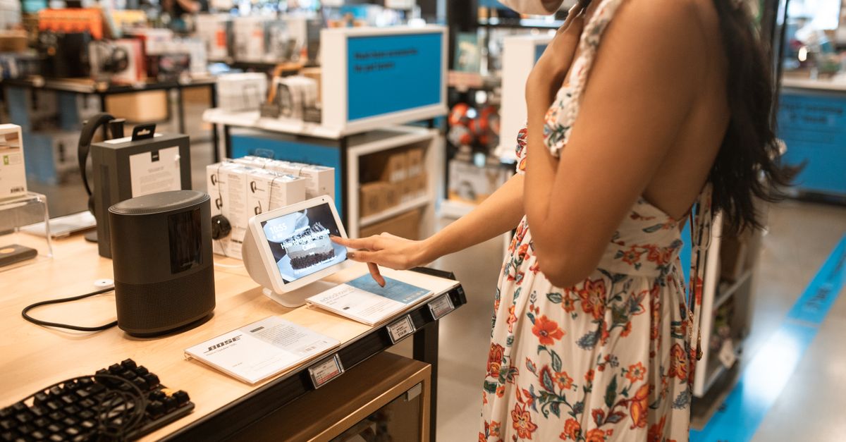 Cómo usar asistentes de IA para comparar compras sin ceder tus datos ni la decisión final tecnología moderna: A woman interacts with a touchscreen display in an electronics store while shopping.