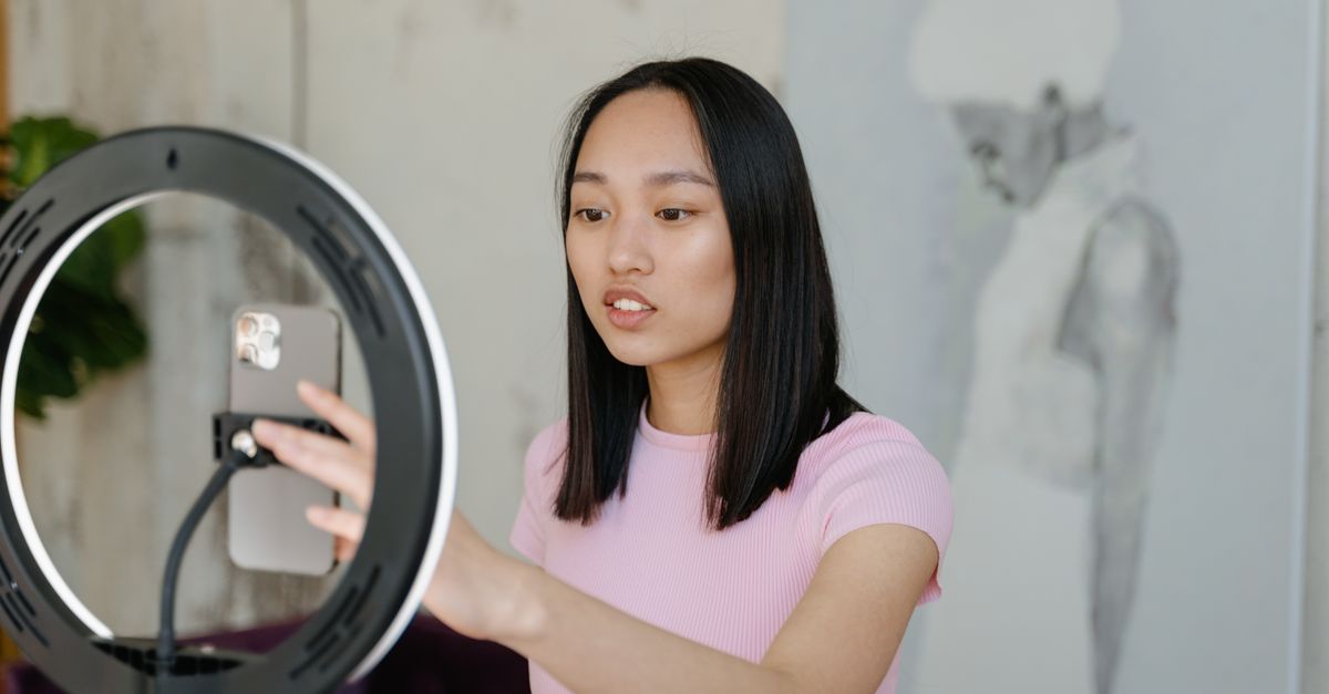 Búsqueda en TikTok, Instagram y YouTube: cómo encontrar información útil sin caer en desinformación social media technology: Young woman using a smartphone and ring light for social media content indoors.